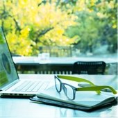 Desk with laptop open, book and eye glasses