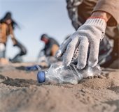 Gloved hand picking recyclable bottles off beach sand