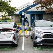 Two electric vehicles plugged into a charger in a parking lot