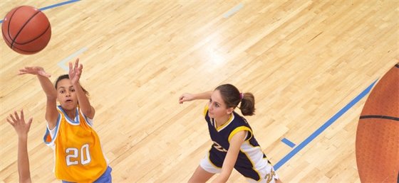 Teenage girl shooting basketball while defender watches.