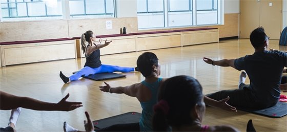 Patrons performing a yoga pose with instructor's direction.