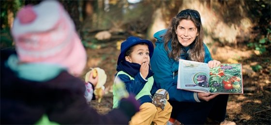 Adult reading a book to children outside