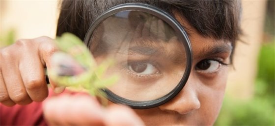 Child looking through a magnifying class at nature