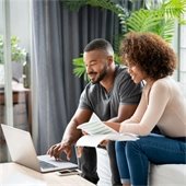 A man and woman sit side by side overlooking paperwork and a laptop