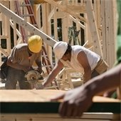 Two male construction workers use a circular saw to cut plywood on a construction site