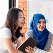 Two women sit side by side in a meeting with a poster board with Post-Its 