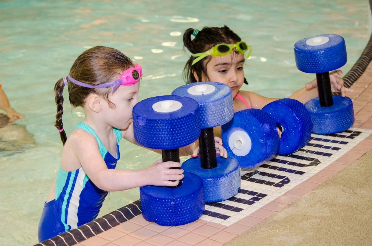 Two children playing with floatation tools in swimming lessons