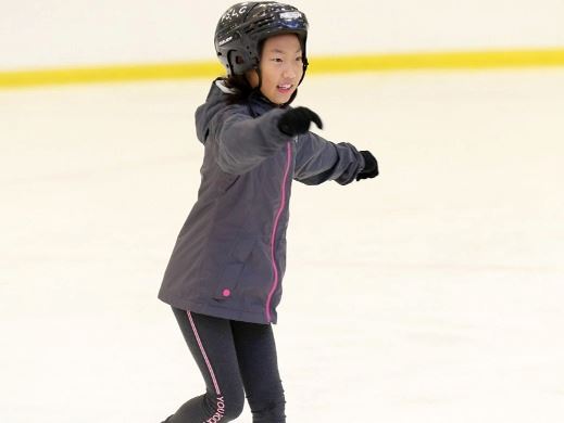A youth wearing a black skating helmet and winter jacket skating in an indoor arena