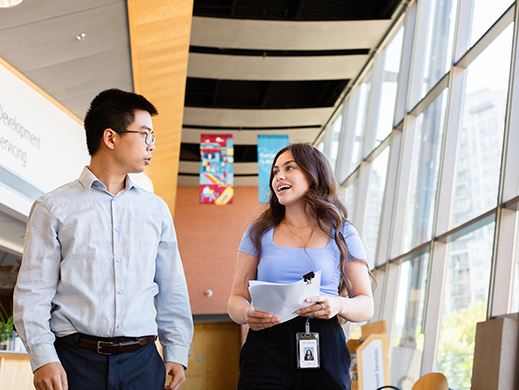 An image of a woman and man walking down a hall in a building talking to one another. 