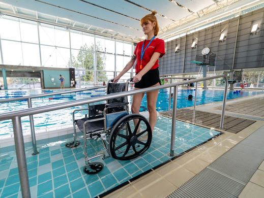 Person standing behind wheelchair beside pool.