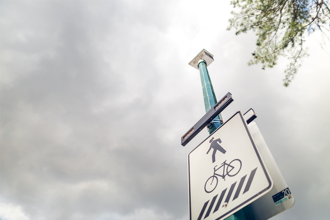 Crosswalk sign with clouds behind it. 