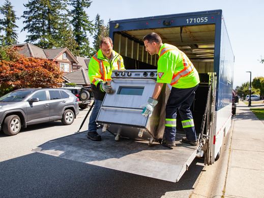 Two people unload a stove from the back of a truck