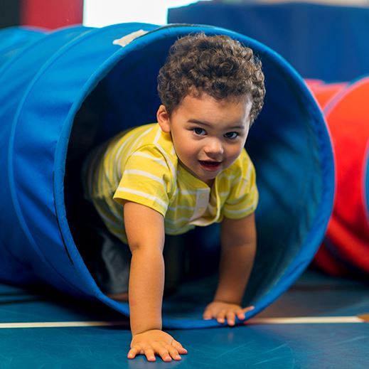 Young boy with curly hair crawling out of a play tent
