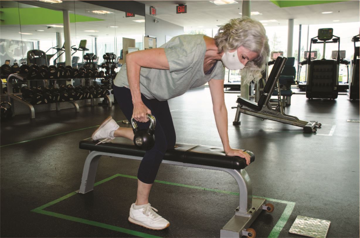 A woman wearing a mask is working out with a kettle bell