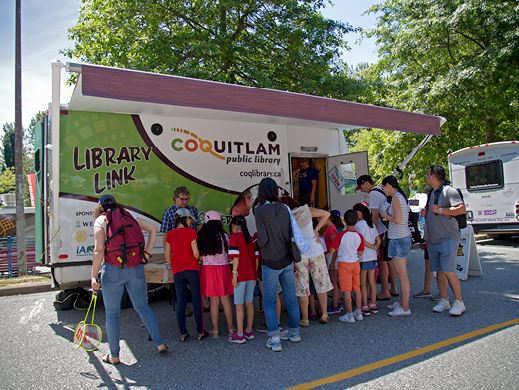 Image of people standing in front of the Library Link mobile library in a park setting.