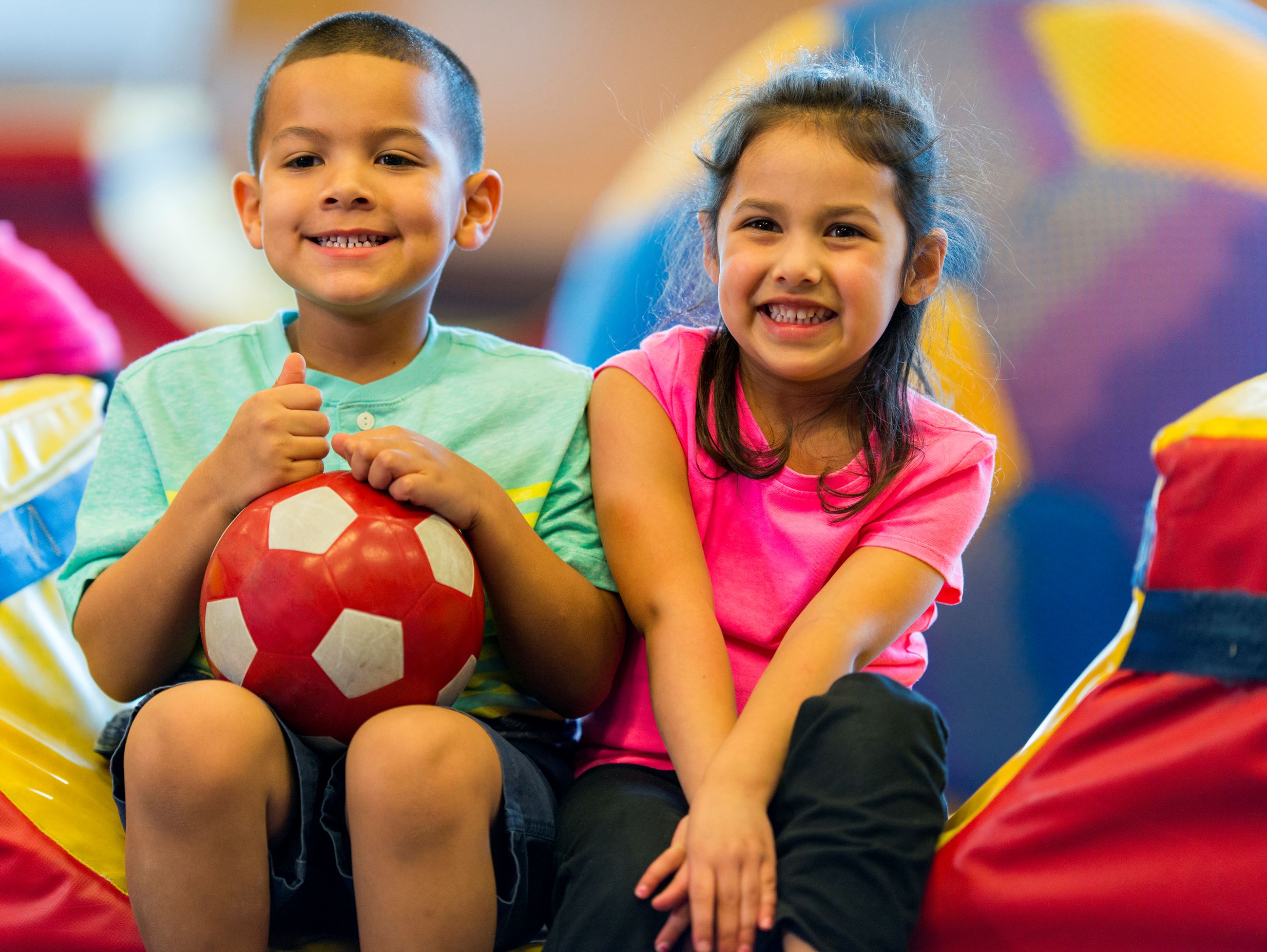 A boy and a girl sit on a piece of play equipment side-by-side. 