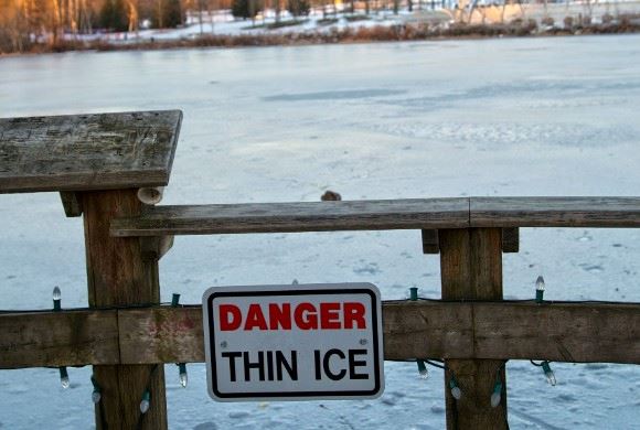 A Danger Thin Ice sign posted on a fence in front of a frozen Lafarge Lake
