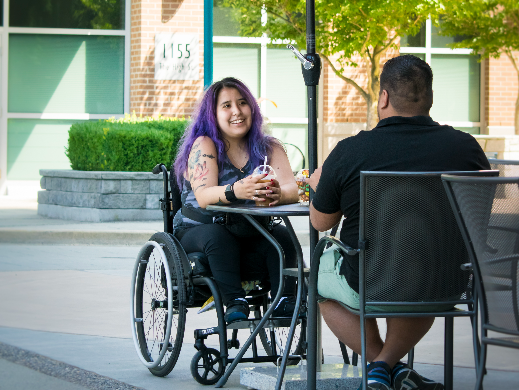 A woman in a wheel chair sits at a table with a man enjoying converstaion