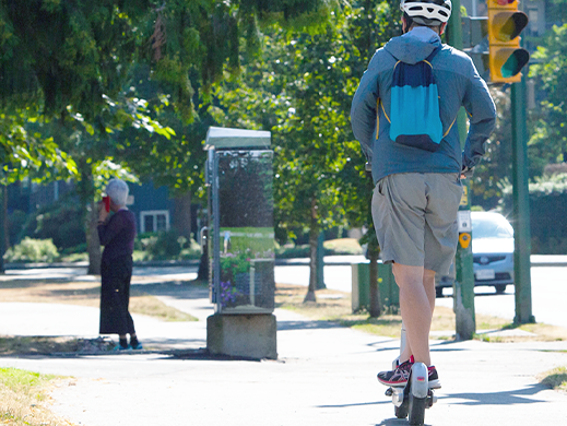 A person wearing a white helmet riding an electric scooter along a pathway