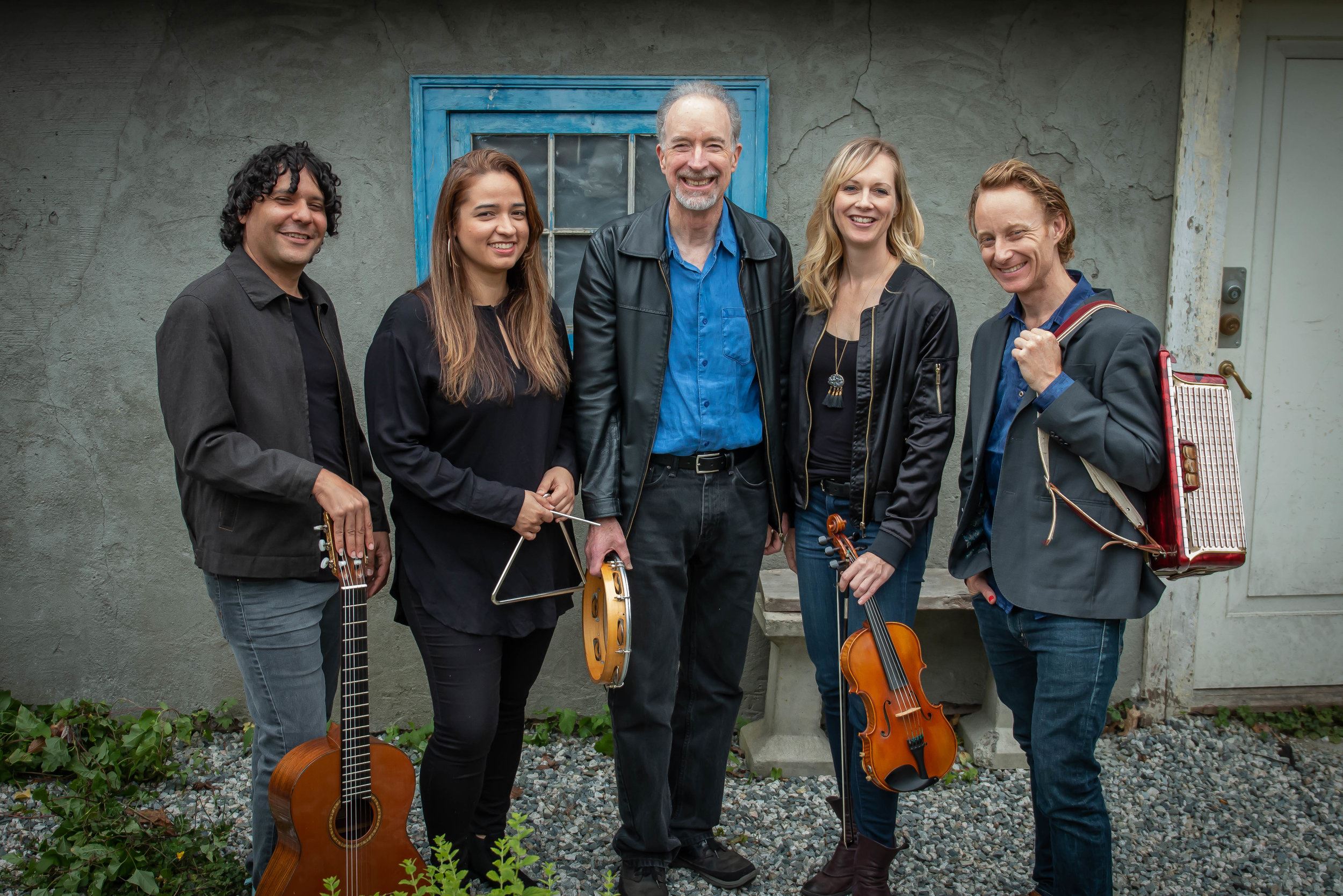 5 members of the band standing in front of an old cottage holding their instruments